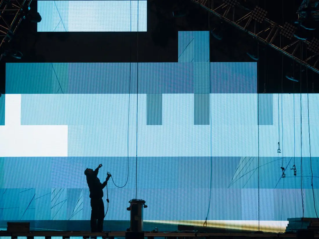 Técnico em silhueta montando um painel de LED na estrutura do evento